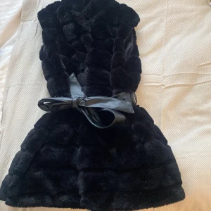 Svart pälsväst - Svart mjuk pälsväst med läderband med två framfickor. Västen är i mycket bra skick, knappt använd. Passar storlek S och M. Västen är ganska lång, går mig (som är 162) över rumpan.          💓Gratis frakt💓