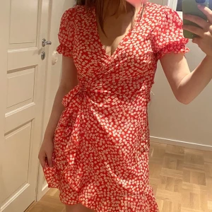 Sommarklänning  - Röd, vit blommig sommarklänning med knyte runt midjan och volanger nedtill med Scrunch på axlarna