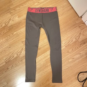Gymshark tights - Grå gymshark tights med rosa band överst. Lappen är bortklippt men skulle tro att det är storlek S/M. Sparsamt använda och i fint skick