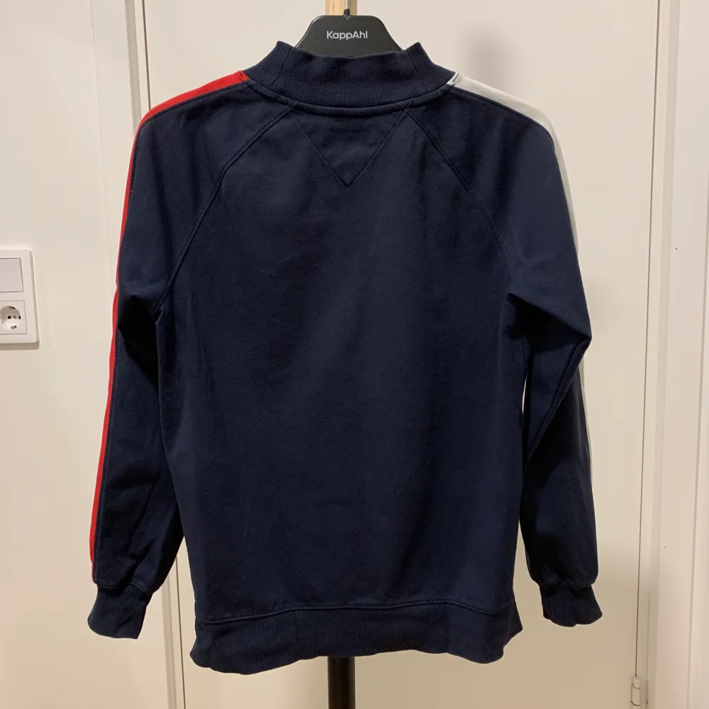 Blå Tommy Hilfiger tröja med ena ärmen röd detalj och andra ärmen vit detalj samt liten logga på bröstet. Tröjan är i använt skick. Storlek S men passar storlekar XS-M. . Tröjor & Koftor.