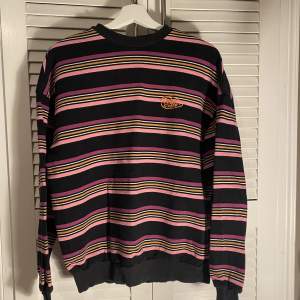 Här är en sweatshirt som är i nästan nyskick, tröjan har många olika färger som svart, orange och lila.