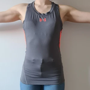 Träningstopp Under Armour - Grått träningslinne från Under Armour, med orange detaljer. Bra kvalité och skönt material.