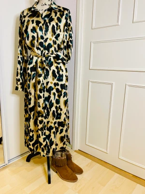 Klänning från VILA - Säljer en  mycket fint klänning med bältet Ian använda som kaftan Färg beige med grön och brun mönster    Felfria  Tyget - poliesyer med silke