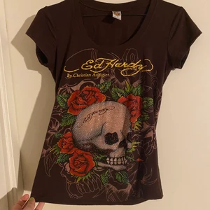 Brun Ed Hardy  t-shirt - Fin Ed Hardy T-shirt. ☠️❤️ I använt men fint skick. Några paljetter har farit av på några ställen. Jag kan skicka flera bilder på tröjan det är bara att skriva ett meddelande. 😊 Står ingen storlek i men jag uppskattar den till S/M. Har köpt den second hand så kan inte garantera att den är äkta. Jag tar swish och skickar spårbart.  💗 