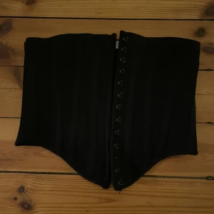 Svart korsett  - Svart midjekorsett med knäppning det framme.