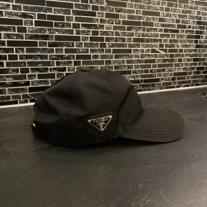 Prada keps - En Prada keps som aldrig användes när den köptes, helt ny. Det är storlek M men går att justera beroende på storleken på ditt huvud. ( priset kan diskuteras ) TAR EMOT BYTEN!!!