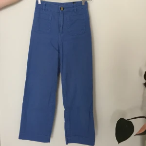 Högmidjade blå byxor från Monki - Högmidjade blå byxor från Monki. Tight passform med raka, svagt utsvängda/vida ben som slutar ovanför ankeln. Köparen står för fraktkostnaden.