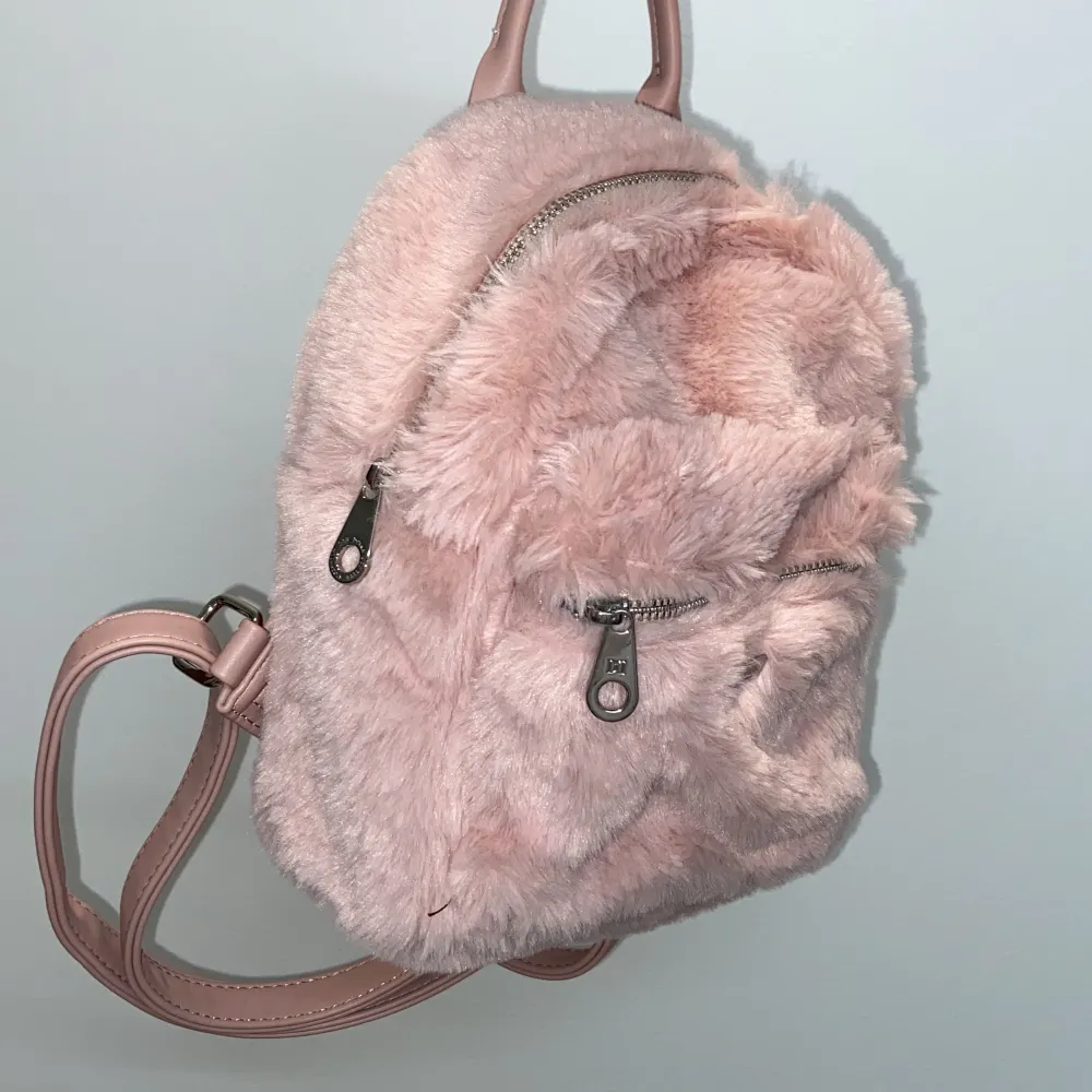 Söt ljus rosa liten ryggsäck, har använt ett fåtal gånger och är i bra skick, det finns ett litet fack på utsidan och ett stort fack med två små fack i, väldigt söt och fluffig.  Ca 25 cm hög och 20 cm bred . Väskor.