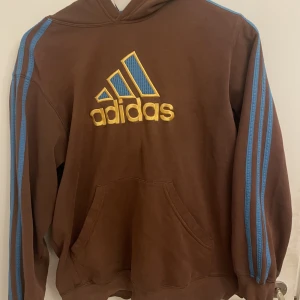 Brun och blå adidas hoodie - Adidas hoodie bra skick inga hål eller synliga märken. Bra storlek för mig som är smal och runt 190cm. Köpt för 430kr på beyond retro