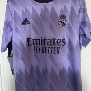 Real Madrid Tröja - Tröjan är i nyskick och har aldrig använts, anledning till det är att tröjan är lite för stör för mig och därför har jag aldrig använt den.   Det finns inga defekter med tröjan då den är i perfekt skick.   Meddela gärna om du har frågor!