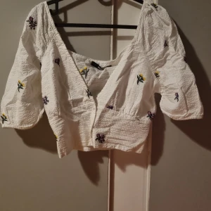 Vit sommartopp - Söt vit sommartopp med lite blommor på. Tunnt och luftigt material och lite stretch vid midjan/ryggen. Keyword LITE stretch. Jättefin och härlig jag upplevde den att den gick lite för långt ner vid brösten för min smak därför säljer jag den