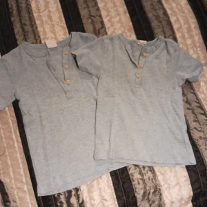 2 t-shirtar i ljusblå barn - 2 t-shirtar i ljusblå med knappar. 1 i storlek 86, 1 i storlek 92. Oanvänt skick