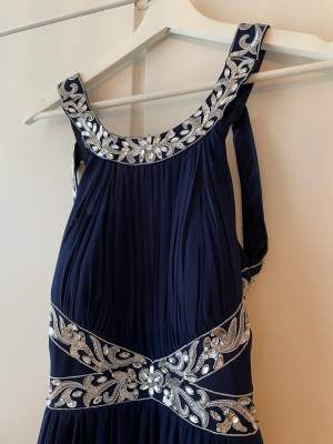 Mörkblå balklänning med öppen rygg och fina detaljer. Gott skick, sparsamt använd. Uppsydd: ca 141-142cm lång från axlarna. 