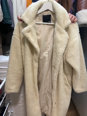 Beige kappa - Säljer denna söta beiga kappan som är varm och mysig pågrund av att den inte kommer till användning. Den är använd fåtal gånger och är i nyskick. 