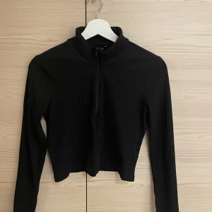 Topp med zip - Svart, ribbad, långärmad topp med halv zip. Från monki. Utmärkt skick!