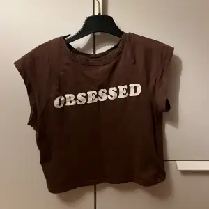 Brun T-shirt med test där det står ”obsessed”. Storlek:Small Bra skick!
