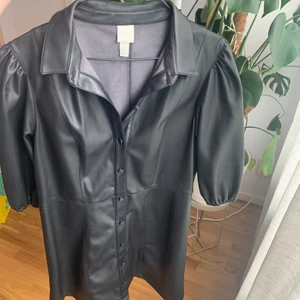 Klänning från H&M storlek 42 - Klänning i skinnimitation från H&M storlek 42. Klänningen har puffärmar samt knappar som går att knäppa hela vägen. Säljer för 120kr