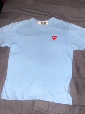 CDG T-shirt - Säljer min CDG tshirt i ljusblå och röd, den är i bra skick och storlek M. Tyvärr för liten och passar inte mig längre (jag är 190cm och den sitter väldigt litet) köpt för ~900kr på NK säljer för 400kr