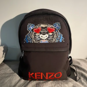 Kenzo ryggsäck - Säljer nu min 4 år gamla Kenzo backpack, köpt för ca 3.000kr på den officiella hemsidan.  Skicket är inte det bästa varav priset, (kan sänka).  Inga större slitage utan rätt normal slitage för åren den har, mest använd för resande.