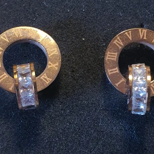 Örhängen bijouterier guldfärgad metal  - Fina örhängen "ring på ring" kommer ej ihåg märke. Köpt på Safira. Fattas ett par stenar därav pris. Fina ändå. 2 cm  Skickas spårbart 29 kr.  Mvh