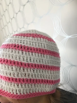 Randig mössa  - Unik virkad rosa och vitrandig mössa med ljusblå blomma längst upp. Liknande kan beställas i andra färger. 