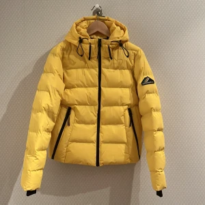 Superdry Gul vinterjacka - Säljer min superdry gula vinterjacka med svarta detaljer. Jackan köptes förra året för 1300kr. Jag använder spårbar frakt via postnord när jag skickar, köparen står för frakten 66kr