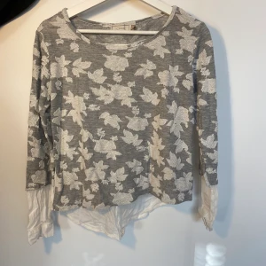 Creme tröja med blommor - En grå tröja med vita blommor och skjort material i ryggen.  Kunden står för frakt, inga byten.