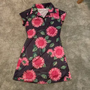En fin siden klänning med svart bakgrund och starkt rosa solrosor på.💕💕Den har en skjortkrage med tre knappar. Min mammas gamla tror den är från 80talet.
