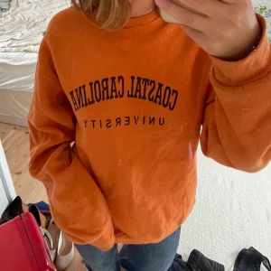 Orange sweatshirt - Sweatshirt i stark orange färg med trycket ”coastal Carolina university”. Köpt på en vintagebutik. Härligt material, bra skick. Säljer då jag har för många sweatshirts.
