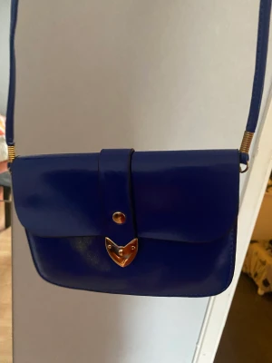 Blå väska - Royalblå väska med gulddetaljer. Smalt och långt band.