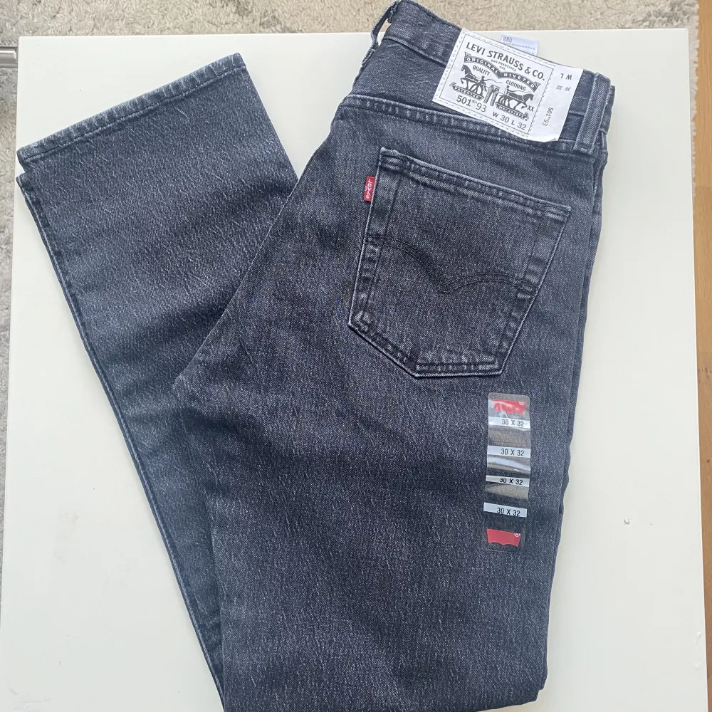 Levis 501 93’ Herrjeans i nyskick med lappar på. Svartgrå jeans, urtvättad svart nyans. Midjemått: 37,5cm  Innerbenslängd: 79,5cm 99% Bomull, 1% Elastan/Stretch. T-shirts.