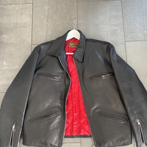 Skinnjacka äkta - Supersnygg Skinnjacka med röda detaljer. Svart med lite lite brunt i! Passar xs-m beroende på passform. Jag har vanligtvis s och den sitter perfekt overzise på mig! 