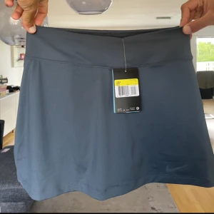 Nike tenniskjol - -Mörk grå/blå tenniskjol   -Helt nyskick.   - Insydda shorts under kjolen givetvis :)  -Säljer pga aldrig kom till användning!