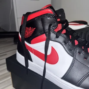 Air Jordan 1 Mid Black/Fire Red-White - säljer ett par feta unisex air jordan 1 mid black/fire red-white, köpta från nike.com (kvitto finns).   de är dead stock och endast använda 2 ggr - som nya!  väldigt rena och fräscha strl. 45 kontakta för mer bilder/frågor  priset kan diskuteras  mvh