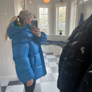 Superfin designad vinterjacka H&M - En  egendesignad vinterjacka från H&M i en superfin lite glansig blå med grönt inuti. Strl xs men rymlig i strl. Säljer på grund av att den tog så lång tid att få så hann att köpa en liknande. 