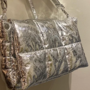 Stand studio väska silvrig  - Stor väska från stand studio, finns både axelrem och handtag som går att ha över axeln. Knappt använd och felfritt skick. 