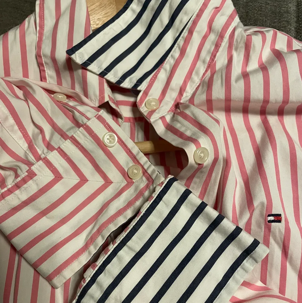 Äkta Tommy Hilfiger skjorta med fina reversibla detaljer, marinblå och rosa ränder. Jättefint skick, som ny. Storlek XS-S, säger stretch men jag tycker att den sitter tajt.. Skjortor.