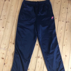 Trackpants  - Ett par mörkblåa trackpants med knappar på sidan från märket fila. Byxorna är väldigt bekväma och i ett bra skick. Säljer dessa för att de är för stora för mig! 100 kr + frakt 