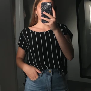 Randig blus - En svart blus med vita ränder och en silvrig dragkedja i nacken. Jag har stoppat in den på bilden så den är lite längre i verkligheten. Aldrig använd och mycket bra skick. 10kr + frakt 44kr (tar bara swish)