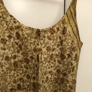 Silkig klänning - * Underbar silkig klänning i gula bruna och gröna toner med justerbara axelband. Passar en M-L. Har en insydd ”underkjol” i samma mönster som resten av klänningen men transparent— vilket ger en vacker flow-y effekt. Knälång på mig som är 174. 