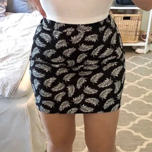 Svart kjol med vita blad - Svart kjol med vita växtblad på. Passar xs/s, köpt secondhand! Frakt tillkommer💓