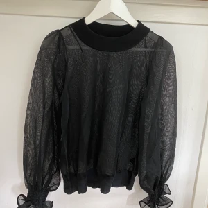Svart H&M topp - Svart sheer topp från H&M trend, perfekt till fest. Resår vid ärmarna och mudden. Använd men i bra skicka. En liten dragning på ärmen (se bild). 