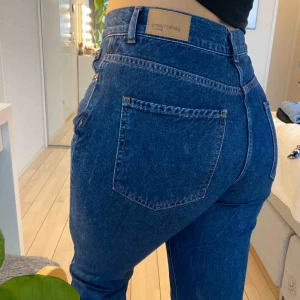 Jeans  - Högmidjade mörkblå mom-jeans från Ginatricot i stl 40 i bra skick!Passar M-L. Har klippt dessa så de slutar lite över ankeln på mig (167 cm). Brons knappar & detaljer, sluts med dragkedja & knapp. Köparen står för frakt💖