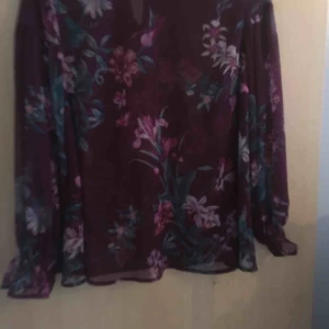  - En rödblommig blus med volanger i hals och armar, använd en gång 