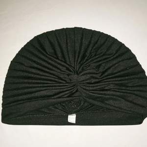 Svart mössa/hatt i turbanmodell, något glansigt material.  Sparsamt använd.  50kr + 20kr frakt. Betalning via Swish. 