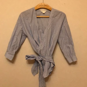  - Jättefin blus från H&M med smala blå- och vita ränder. Knytning runt midjan. Storlek 34. Frakt tillkommer!
