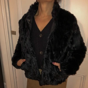 Pälsjacka  - Svart jacka i pälsimitation med krage och har knappar att stänga jackan med. 