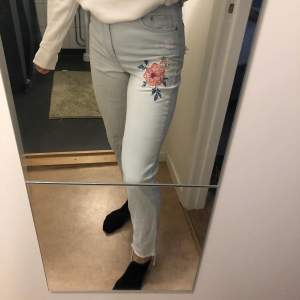 Ljusa jeans med rosa blommor på två ställen och slitningar nertill samt på en bakficka. Raka i benen och hög midja. Jag är 172 lång. Frakt tillkommer! 