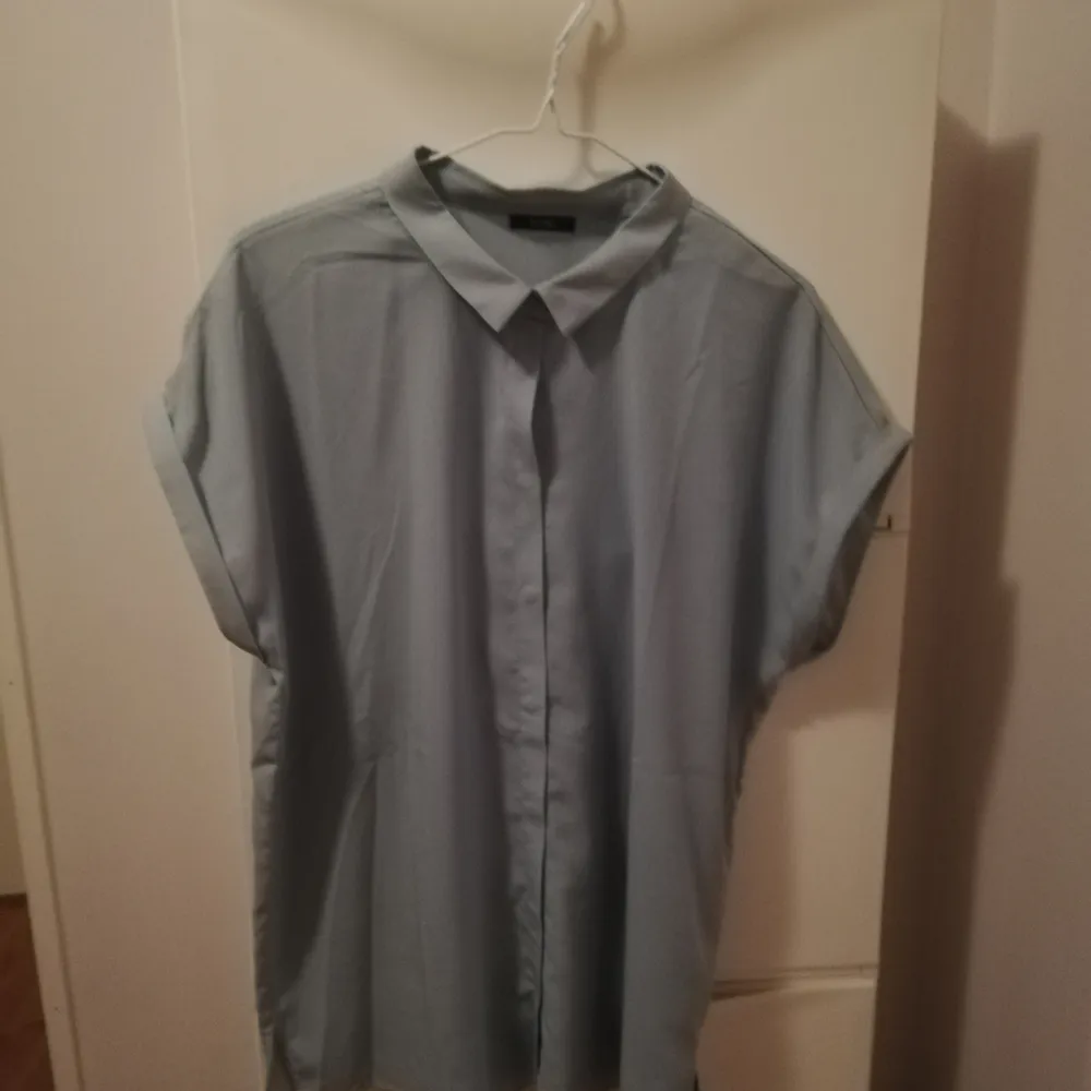 Lös, boxig blusskjorta med vikta korta ärmar och dolda knappar från Kiomi strl 42. Färgen är svår att beskriva, men närmast är nog mycket ljus grön/grå. Endast använd en gång, passar inte mig längre. Du står själv för fraktkostnad. . Blusar.