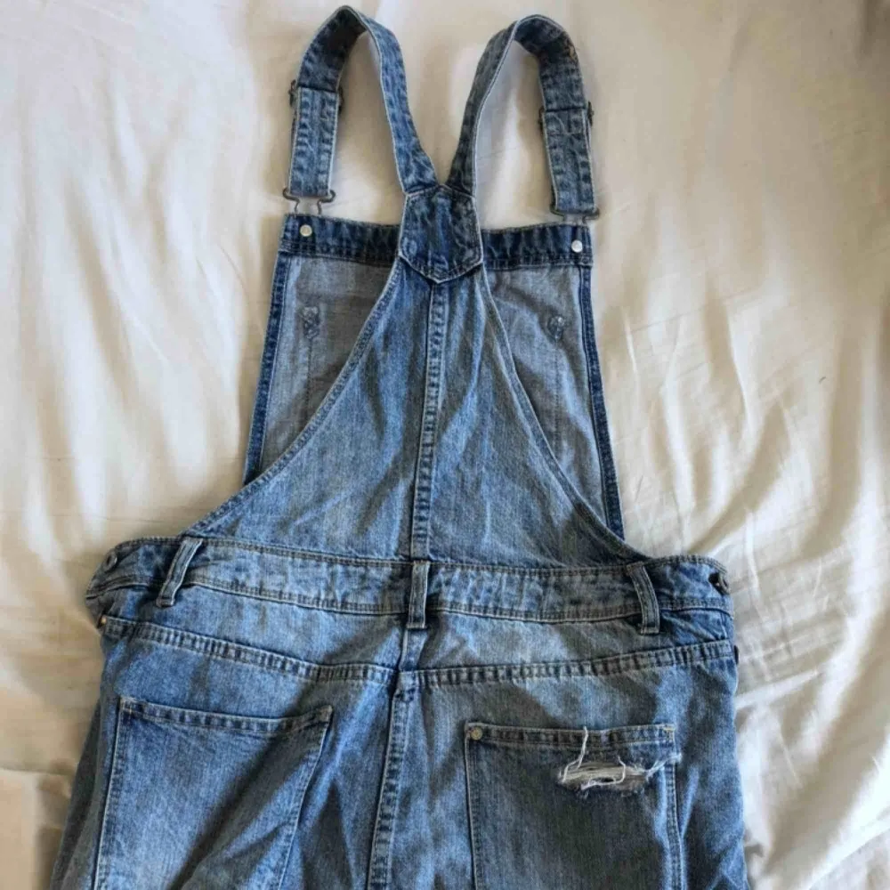 Säljer den superfina jeans-hängselklänningen på bilden. Bra skick, säljer pga att den inte används tyvärr. Den har knappar på båda sidorna av höfterna och justerbara axelband.. Klänningar.
